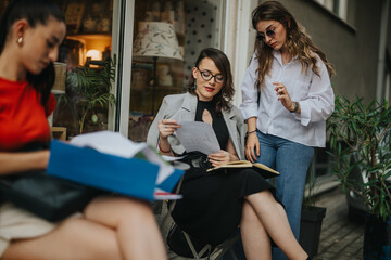 Three businesswomen holding a meeting outdoors, focusing on reviewing and discussing documents. Collaboration and teamwork in a professional setting.