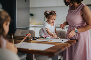 Fototapeta premium Young mother spending quality time drawing and painting with her little daughters at home, fostering creativity and bonding.