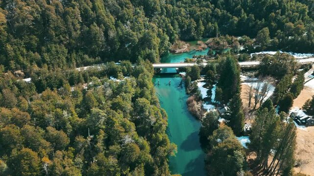 A breathtaking aerial view of a tranquil landscape in Patagonia, Argentina. The scene showcases a lush forest, a calm blue lake, and a meandering river, all framed by verdant greenery. The natural bea