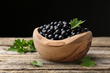 Ripe black currants and leaves in bowl on wooden table