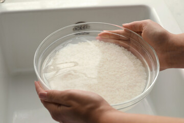 Woman holding bowl with rice and water above sink, closeup
