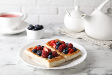 Tasty puff pastries with berries and tea on white marble table