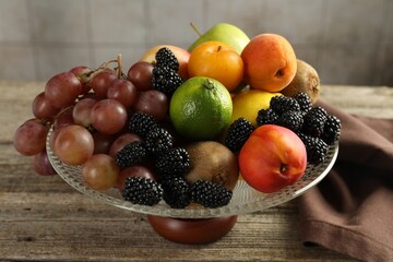 Glass vase with different fresh fruits and berries on wooden table, closeup