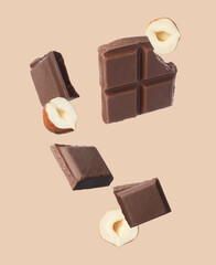 Pieces of tasty chocolate and hazelnuts in air on dark beige background