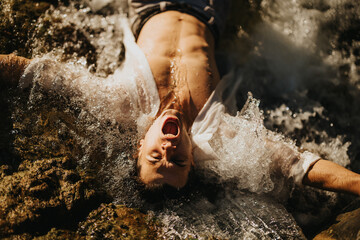 Man experiencing the exhilarating sensation of waves crashing over him on a rocky shore, representing freedom and adventure