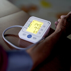 Closeup of a digital blood pressure monitor showing a reading, with a person's arm in view, highlighting healthcare and medical diagnostics.