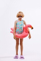 A child in black glasses and a blue-orange swimsuit with an inflatable duck ring on a white background. The concept summer holiday on the beach or pool.