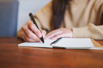 Closeup image of a woman writing on a notebook on wooden table