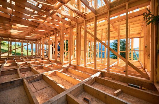 Under-construction residential wooden frame home located near a forest. Commencement of a new construction project for a cozy house or a mountain cottage. Idea of contemporary ecological construction.