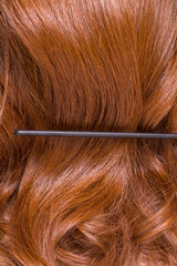 Close-up of dark hair in the foreground. The hair is long and shiny and a comb is used to style it. Hair care and hygiene.