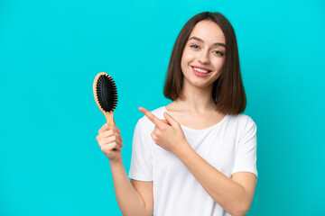 Young ukrainian woman with hair comb isolated on blue background and pointing it
