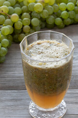 Freshly blended thick grape drink with seeds and pieces of skin, perfect for boosting the immune system. Homegrown white grapes behind.