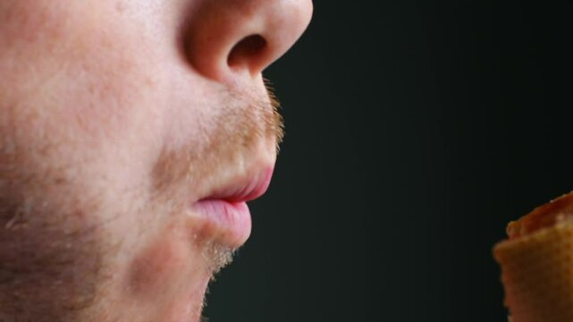 Young man takes big bite of hot dog on black background. Guy savors burst of flavors from juicy sausage soft bun and tangy condiments closeup