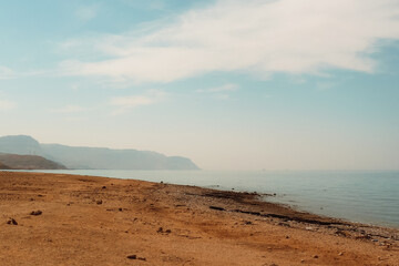 Daytime view of Al Ain Al Sokhna beach, Suez, Egypt. The calm shoreline stretches with mountains in the distance under a clear sky.