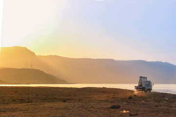 Sunset at Al Ain Al Sokhna, Suez, Egypt, with a truck driving along the beach. Mountains and soft sunlight create a tranquil backdrop
