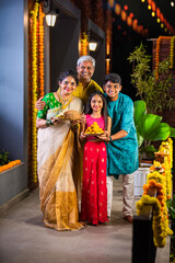 Obraz premium Indian parents with children celebrating Diwali on the balcony, holding Pooja thali and sweets.