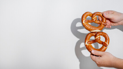 Two pretzels held by Caucasian hands against a plain background, symbolizing traditional German...