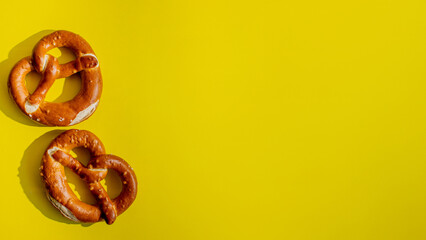 Two freshly baked pretzels on a vibrant yellow background, perfect for celebrating Oktoberfest or highlighting German cuisine concepts