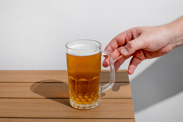 A person's hand reaching for a glass of cold beer on a wooden table, symbolizing relaxation and Oktoberfest celebration