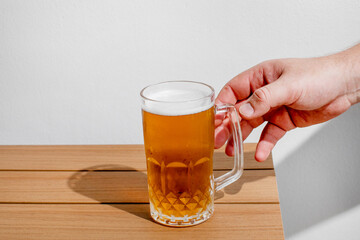 A hand reaches for a frosty glass of beer on a wooden table, symbolizing relaxation and enjoyment during Oktoberfest