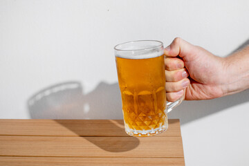 Hand holding a frosty beer mug on a wooden table, perfect for Oktoberfest celebrations or summertime refreshment themes