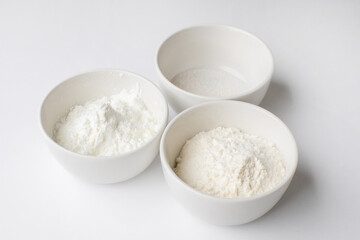 Three white bowls filled with various baking powders on a white background, symbolizing essential ingredients for holiday baking