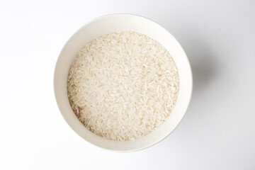 A ceramic bowl filled with uncooked white rice on a white background, optimal for illustrating concepts of basic nutrition or Asian cuisine preparation