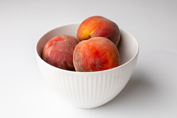 A white bowl filled with fresh, ripe peaches symbolizing summer harvest and nutritious eating on a white background