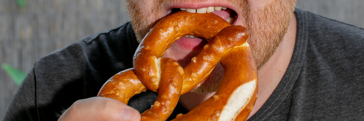 Man enjoying a large pretzel during Oktoberfest celebrations, highlighting the traditional German festival and culinary delight