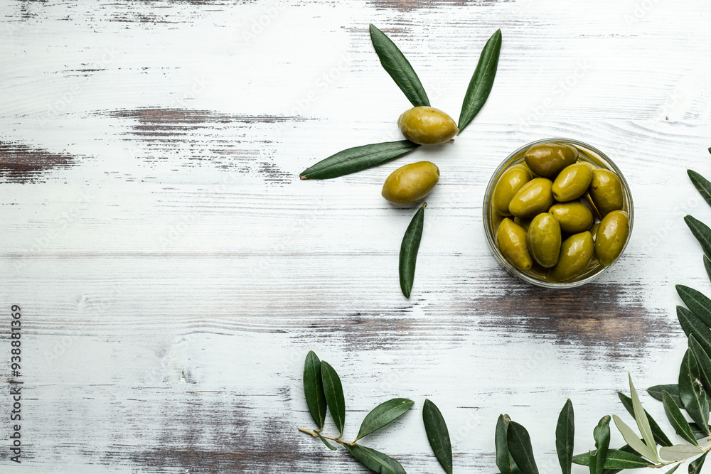 Wall mural greens olives on a white wooden background. olives in bowls and olive oil with fresh olive leaves. c