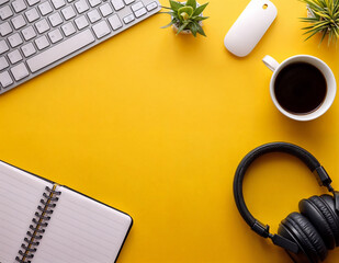 top view of accessories on computer table with keyboard headphone and stationeries on yellow table background.