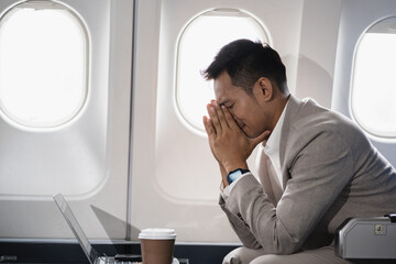 Stress businessman is sitting in the airplane, under stress from working.