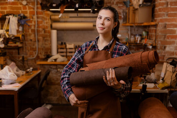 Fototapeta premium Happy young woman craftsman hold leather rolls on atelier workshop