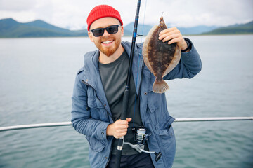 Happy Scandinavian fisherman caught flounder fish with fishing rod, trip Kamchatka Russia....