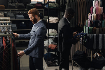 Two mans buyers in fashionable suit chooses jackets and tie in men clothing store