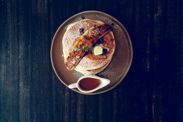 Banana pancakes breaksfast with Mapple syrup on a ceramic plate with a caramelized banana as a decoration on a black wooden table