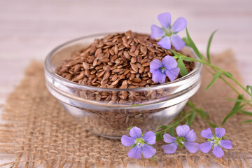Flax seeds in a glass bowl and fresh flax flowers.Close-up.
