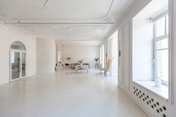 bright interior design of spacious living room with white walls and decorative unique historical moldings on ceiling stylish modern furniture in warm colors without people daylight through the windows