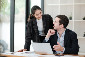 A woman and a man are sitting at a desk with a laptop in front of them