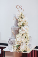 A three tier wedding cake with white flowers and a heart shaped decoration on top