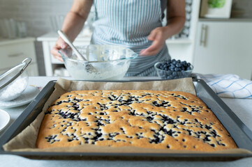 Homemade blueberry sheet cake fresh and homemade baked. Served by a woman with apron in the kitchen
