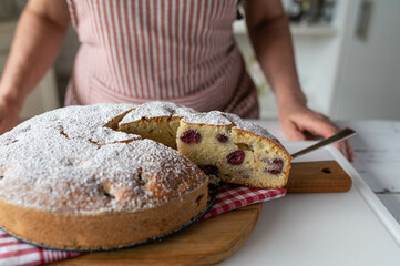 Woman serving a fresh and homemade baked cherry cake in the kitchen