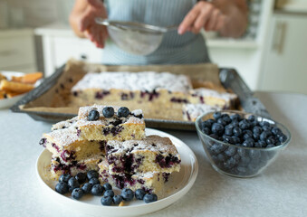 Woman in the kitchen with a fresh homemade baked sheet cake with blueberries on kitchen counter