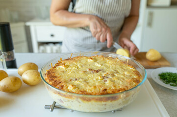Woman in the kitchen with a fresh baked potato casserole on kitchen counter