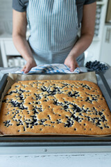 Woman in the kitchen with a fresh baked sheet cake with blueberries on a baking tray