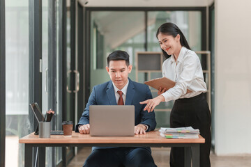 A woman is pointing at a laptop screen while a man looks on. The woman is wearing a white shirt and black pants