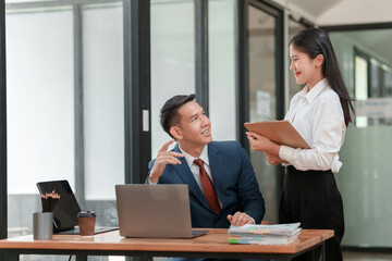 A man and a woman are in a conference room, the man is smiling and the woman is holding a clipboard