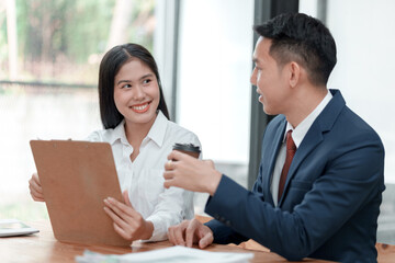 Two people are sitting at a table, one of them holding a clipboard. They are smiling and seem to be having a good time