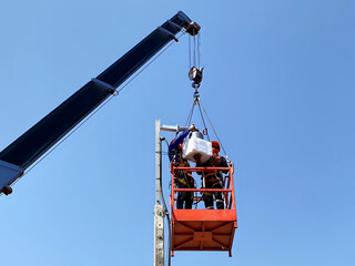 The crane lifting personnel baskets with two worker for CCTV installation at high pole.