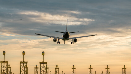 Backview of an airplane landing on Brussels airport during sunset. Runway lights in the foreground. Travel, transport theme. Big jetliner during landing at the airport.